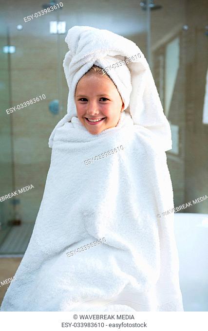 Portrait of cheerful girl wrapped in towel sitting on bathtub
