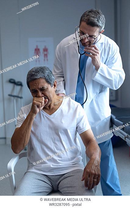 Front view of Caucasian male doctor examining senior mixed-race male patient with stethoscope in hospital