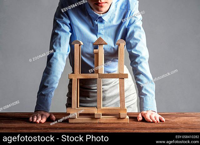 Business woman building construction on table from wooden blocks. Strategy planning and company development. Young woman wearing formal wear sitting in office...