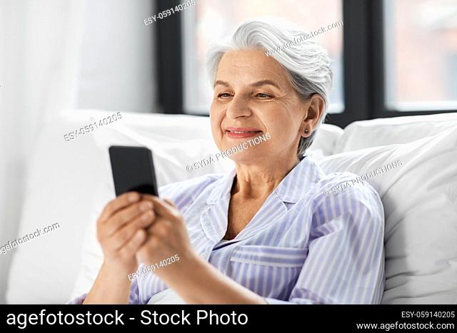 happy senior woman using smartphone in bed at home
