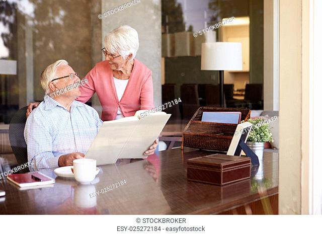Senior Couple Looking At Photo Album Through Window
