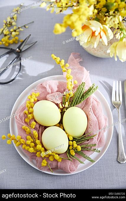 An Easter table with coloured eggs in a muslin nest