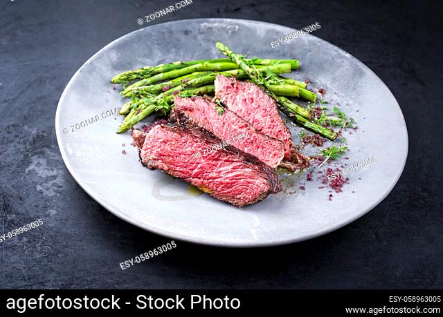 Barbecue dry aged wagyu rib-eye beef steak with green asparagus and red wine salt as closeup on a modern design plate