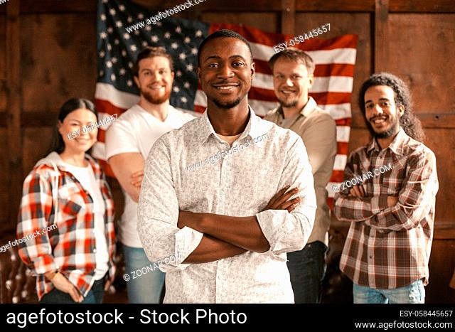 Smilling Multi-National Group Of Young American Patriots Poses Against The Background Of A Wooden Wall With American's Flag