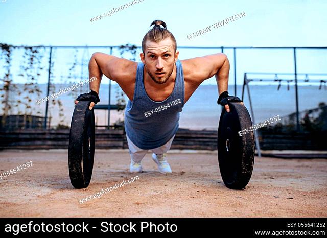 Athletic man doing push-up exercise with weights, street workout, crossfit. Fitness training on sports ground outdoor, male person pumps muscles
