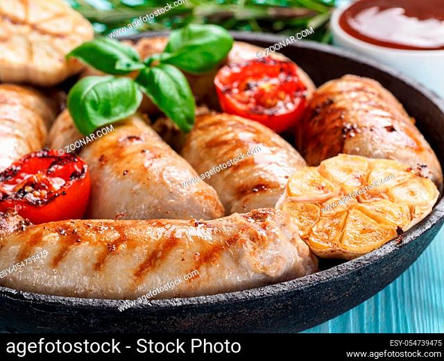 Chicken homemade sausages, sauces ketchup and vegetables and herbs on blue wooden background. Grilled sausages and grilled vegetables in black iron pan
