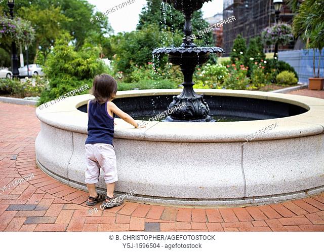 Small child leans on a park water fountain to get a better look