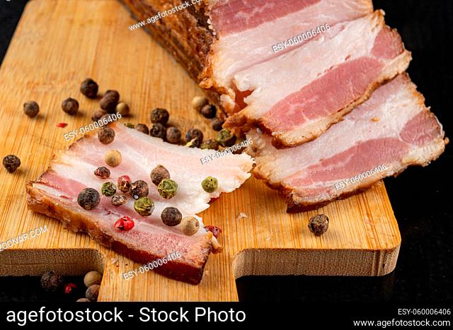 A delicious smoked piece of bacon on a chopping board. A piece of smoked meat from a pig in the kitchen. Dark background