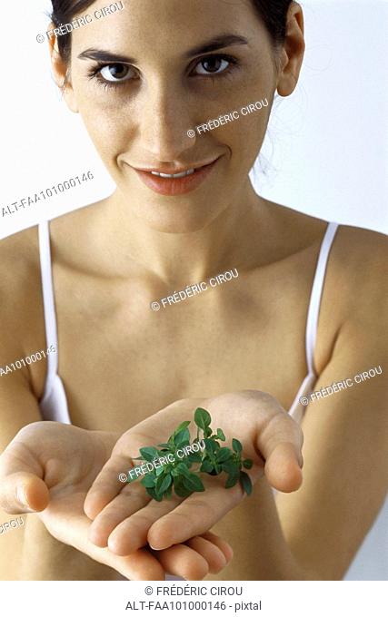 Young woman holding handful of fresh thyme, smiling at camera