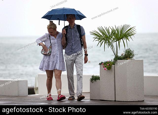 RUSSIA, SOCHI - JULY 9, 2023: A couple stroll with an umbrella as rain falls over the Mayak beach. Last night's storm brought some 80mm of rain to Sochi