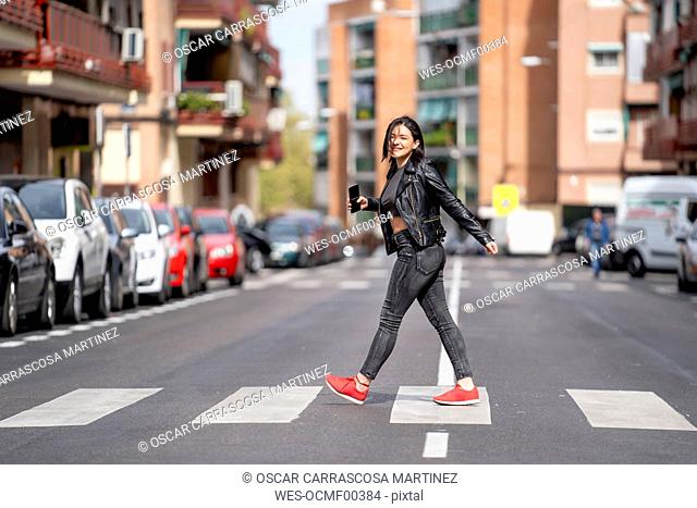 Young woman crossing the pedestrian crossing and using mobile phone