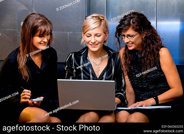 Team of happy young businesswoman having a meeting, using laptop computer, smiling