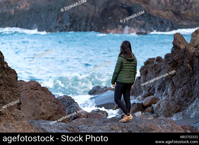 Woman seeing waves crashing on a rocky beach at Seixal, Madeira