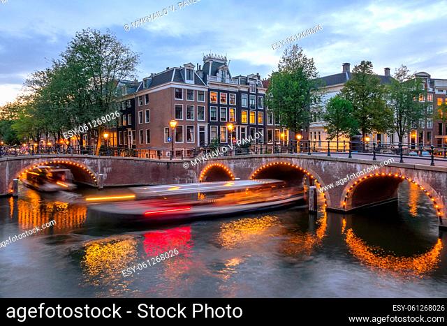 Netherlands. Summer evening on the canals of Amsterdam. Tourist boats sail under the bridges. Traditional houses and bicycles on the waterfront