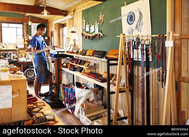 Japanese man wearing blue apron and glasses standing in a leather shop