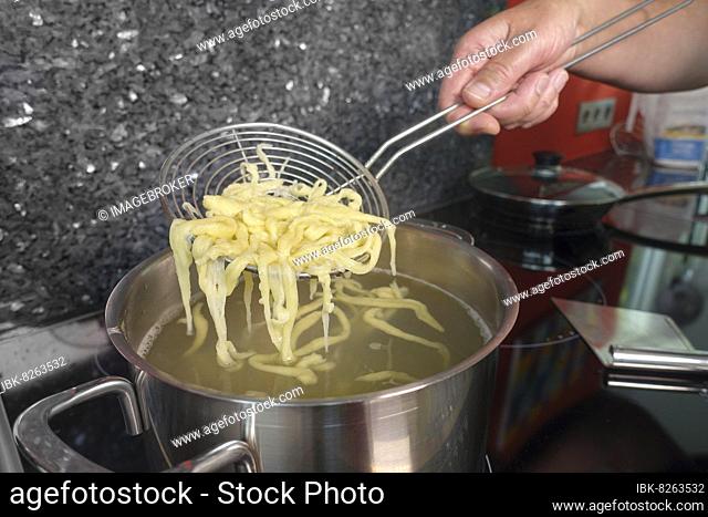 Swabian cuisine, preparing hand-scraped spaetzle for spaetzle casserole, three kinds of spaetzle, removing spaetzle with red pepper from cooking water with a...