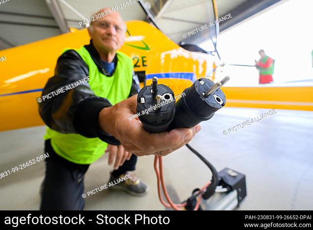 31 August 2023, Lower Saxony, Hanover: Test pilot Uwe Nortmann shows a voltage converter in front of the ""Elektra Trainer"" e-airplane at Hannover Airport