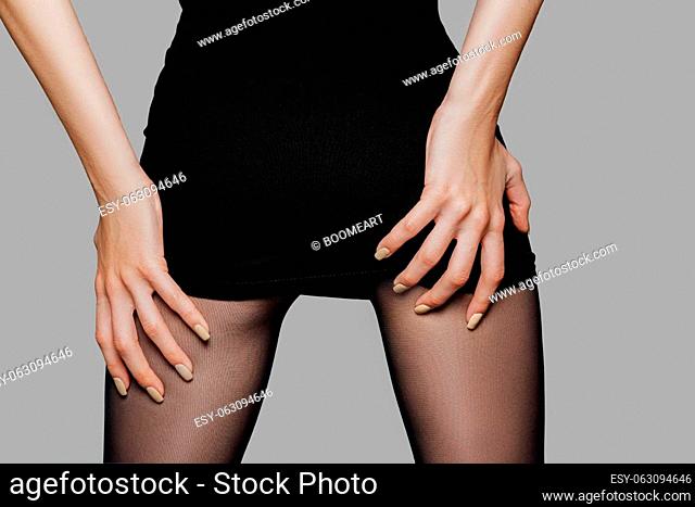 Closeup picture of female back in short black dress with hands on her buttocks. Lifting dress