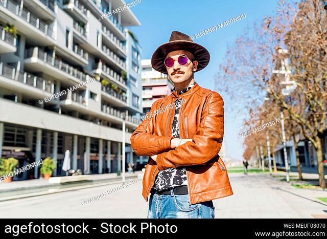 Man wearing hat looking away while standing on footpath during sunny day