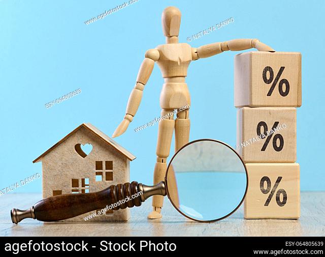 Wooden dummy, house and a magnifying glass, representing the concept of real estate purchase, rental growth, and mortgage interest