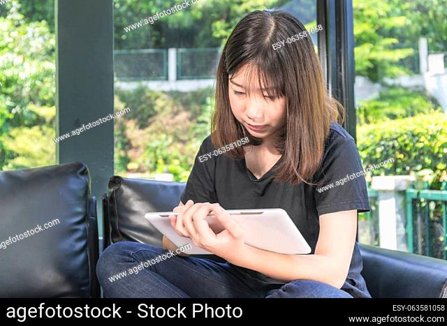 Young girl studying online from digital tablet on the sofa in parlor at home