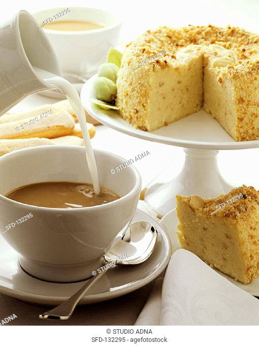 Cup of coffee with milk being poured into it & almond cake