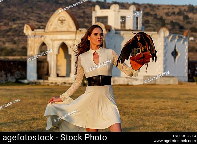 A gorgeous Hispanic Brunette model poses outdoors with a falcon outdoors at a hacienda