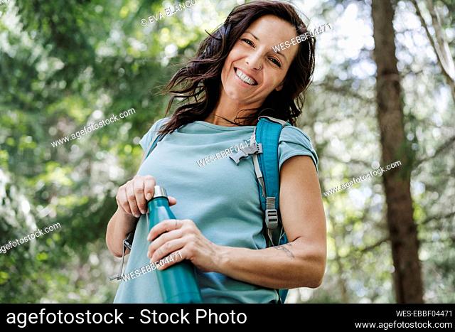 Happy female tourist holding water bottle while standing in forest