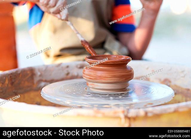 Hands of young potter, creating an earthen jar on the circle, close-up
