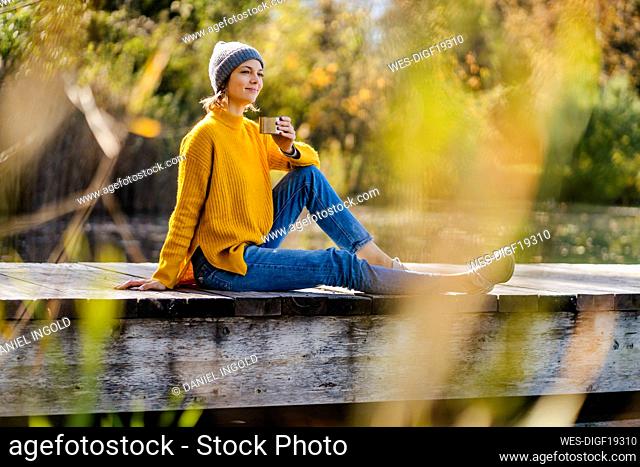 Smiling woman with coffee cup sitting on jetty