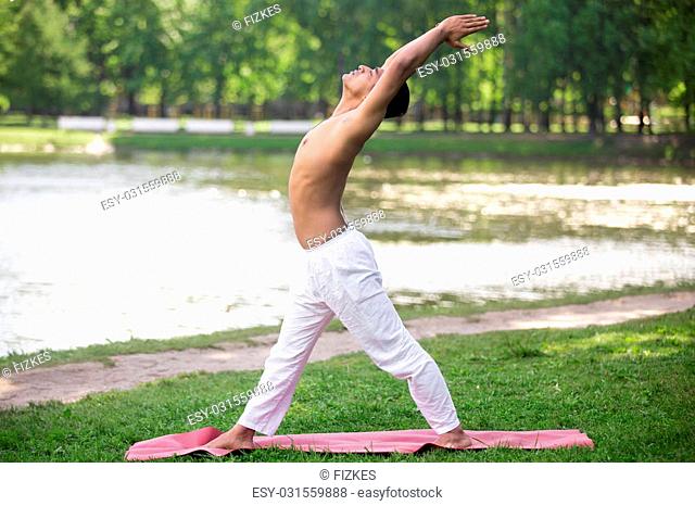 Sporty asian young man working out on grass in park, doing yoga, fitness, pilates training, preparation and variation of Warrior 1, VeerBhadra I pose
