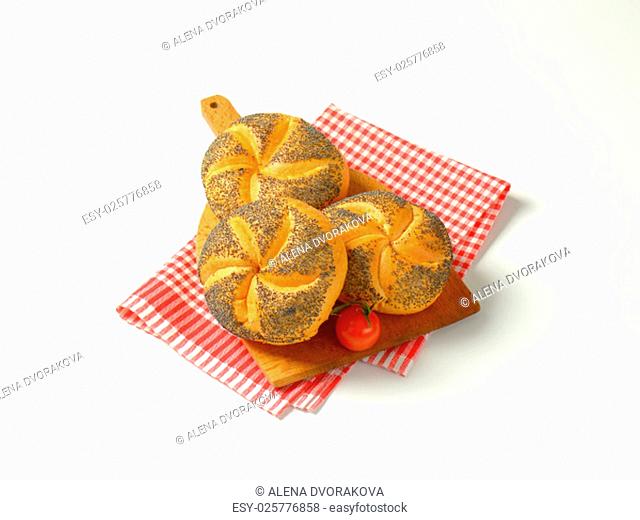 fresh poppy seed buns on wooden cutting board and checkered dishtowel