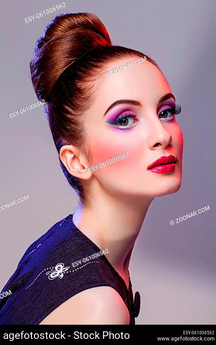 Beautiful young woman with hairdo and bright purple tone make-up. Doll style. Beauty shot on grey background. Copy space