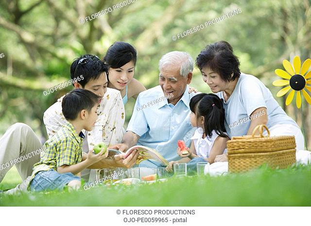 Family outdoors at park having picnic and looking at book