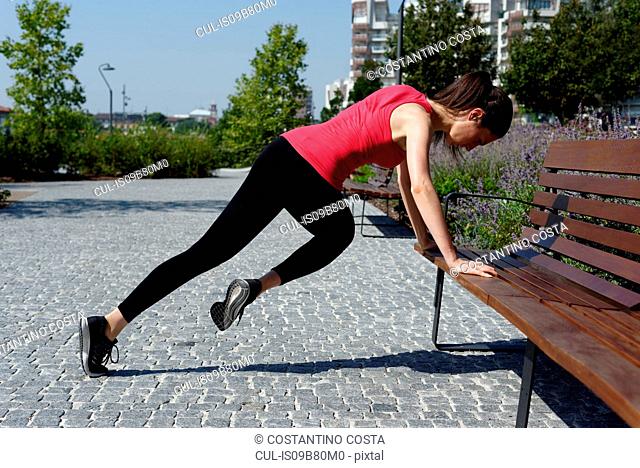 Young woman outdoors, exercising with hands on bench