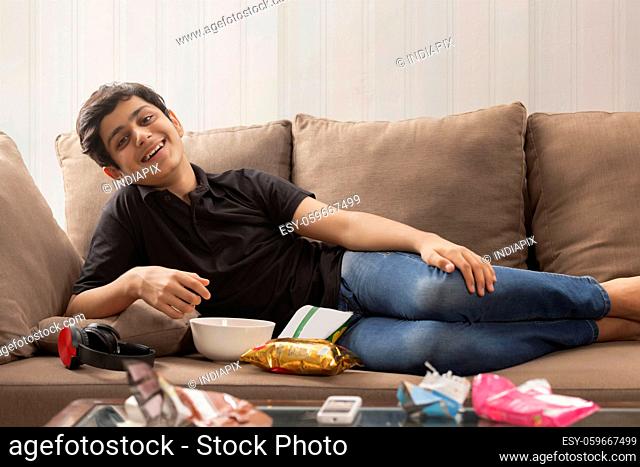 A HAPPY TEENAGER RELAXING ON SOFA AND ENJOYING IN FRONT OF CAMERA