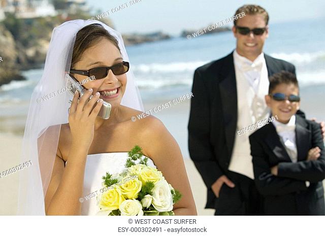 Bride using mobile phone Groom and brother in background