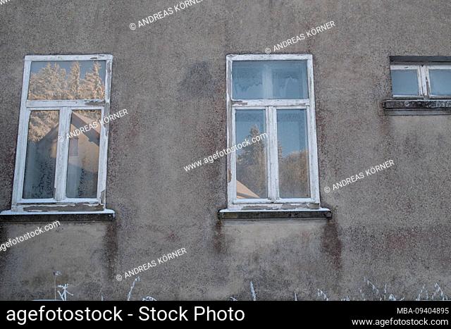 Old windowpane with frosted flowers and reflection of a sunny, wintry landscape and hut in gray facade in Vosges, France