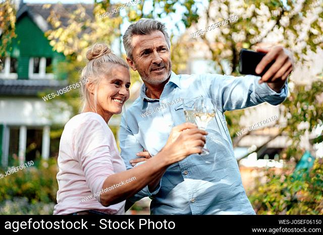Smiling man taking selfie with woman through mobile phone at backyard