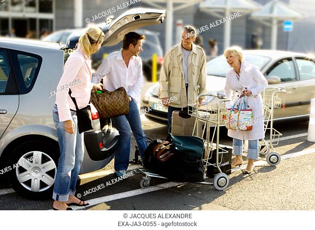 Senior couple and young couple putting luggage in car