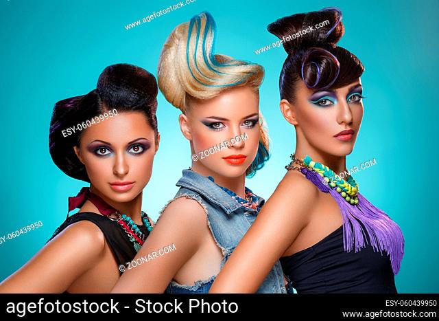 Three beautiful young women with fancy hairstyles and bright makeup. Beauty shot over blue background. copy space