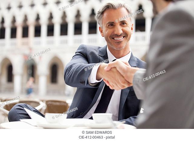 Smiling businessmen shaking hands at sidewalk cafe