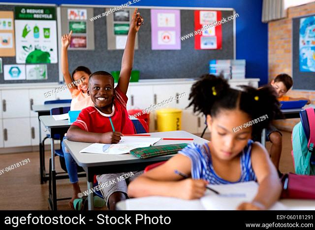 African american boy and girl raising their hands while sitting in the class at elementary school