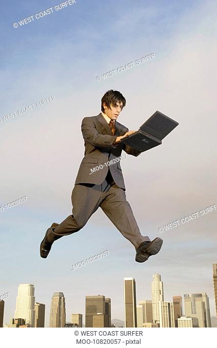 Business man using laptop mid-air above city