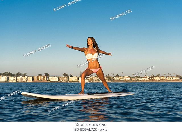 Young woman practicing yoga position on paddleboard, Mission Bay, San Diego, California, USA
