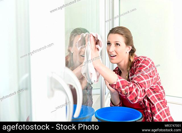 Portrait of smiling woman cleaning the window glass with cloth