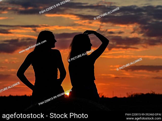 08 August 2022, Brandenburg, Jacobsdorf: Two girlfriends are sitting in a field at sunset. Photo: Patrick Pleul/dpa. - Jacobsdorf/Brandenburg/Germany