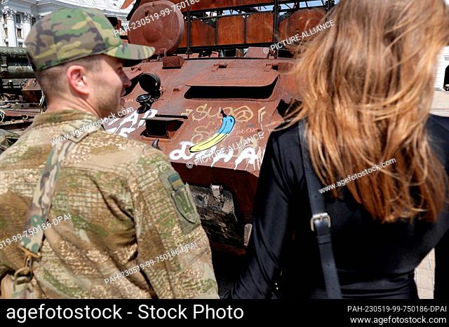 18 May 2023, Ukraine, Kiew: A young couple stands in front of a downed Russian tank, on which the Cologne artist and banana sprayer, Thomas Baumgärtel