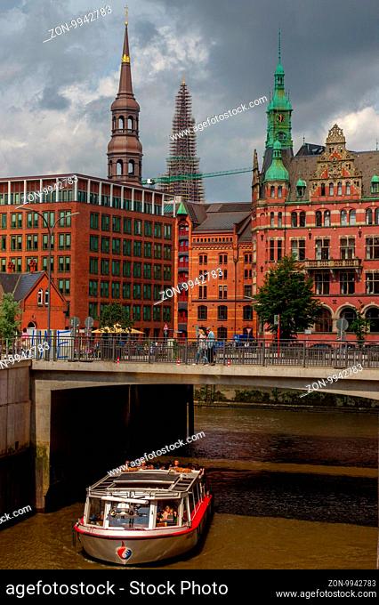 HAMBURG, GERMANY - JULY 18, 2015: a ferry on the canal of Historic Speicherstadt houses and bridges at evening with amaising skyview over warehouses
