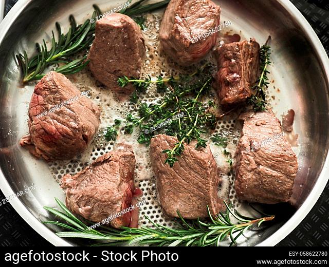 Organic beef fillet with fresh rosemary and thyme in a stainless steel pan, view from above, cooking with fresh herbs, organic food or healthy eating concept